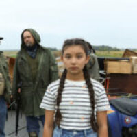Titel: Beans von Tracey Deer – Gewinner des Gläsernen Bären für den besten Langfilm der Kinderjury Beans (Kiawentiio) ist der Kurzname von Tekahentahkhwa, einem indigenen Mädchen und ihre Geschichte spielt 1990 in Kanada während der sogenannten Oka-Krise. Das Mohawk Volk, ein Indigener Stamm, wehrt sich gegen die Erweiterung eines Golfplatzes auf Mohawk-Land. Zu Beginn der Geschichte sehen wir Beans, wie sie gerade ein Bewerbungsgespräch in einer elitären Schule führt. Die Chancen stehen gut, doch dann fragt die Schulleiterin über ihre zwei Berufswünsche angegeben hat. Beans und ihre etwas jüngere Schwester Ruby (Violah Beauvais) sind gemeinsam mit ihrer Mutter gerade in einem Waldgebiet angekommen, wo die Mohawk friedlich demonstrieren und ihre Barrikade aufrechterhalten. Die Mädchen sollen etwas Holz sammeln für ein Feuer sammeln und streifen dazu durch den Wald, wo sie auch durch eine alte Grabstätte der Mohawk streifen. Liebevoll dekorieren sie die alten Grabsteine mit Blumen und beseitigen diverse Golfbälle, […]