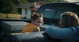 Ein Kind sitzt auf der Ladefläche eines Pickup und blickt zu seiner Großtante